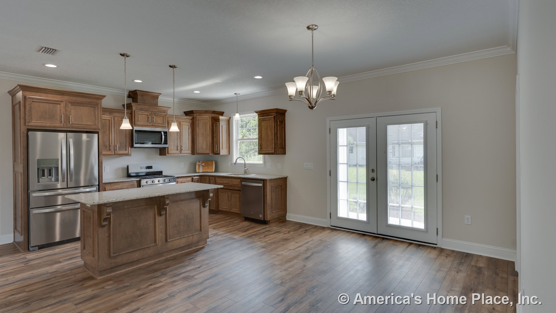 Wood cabinetry kitchen with granite island countertop, stainless steel refrigerator, range, microwave, and dishwasher; pendant lights hang above island, double French doors, crown