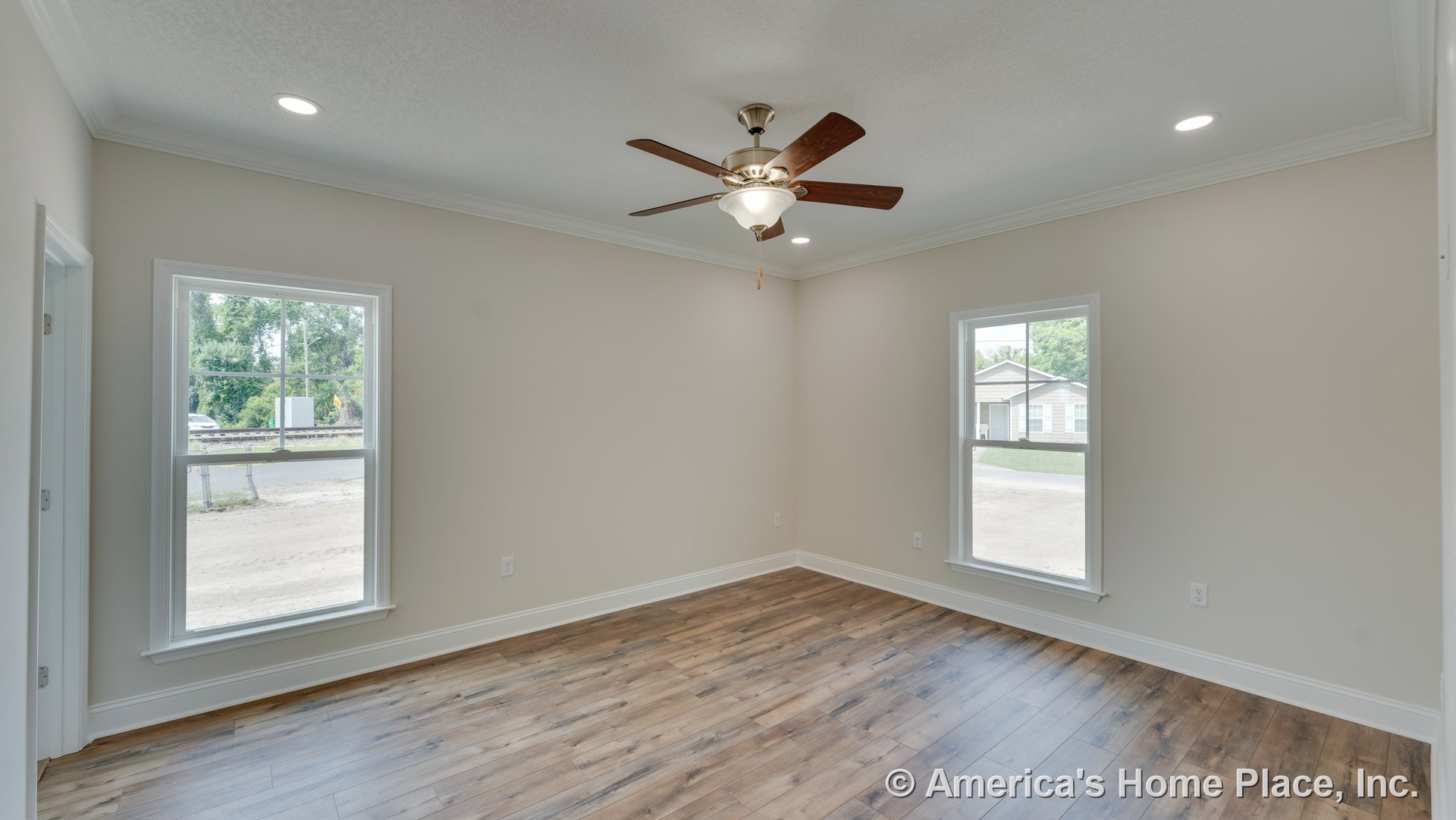 Wood-look plank flooring, neutral walls with white crown molding and baseboards, two large double-hung windows, ceiling fan with integrated light fixture, recessed ceiling lights