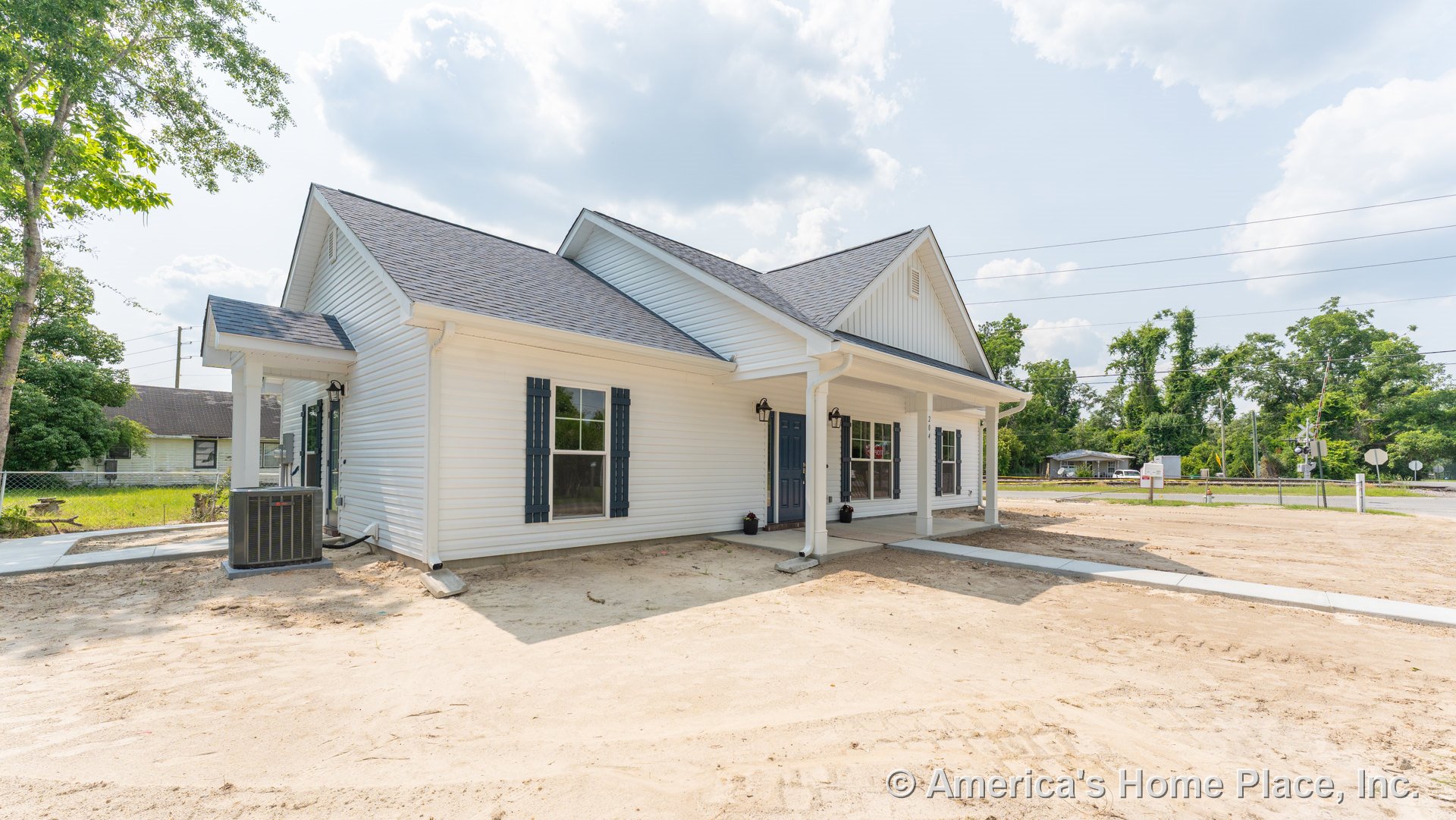 White vinyl siding exterior with blue accent shutters, covered front porch beneath a gabled roof, double front windows, exterior wall-mounted lighting, and decorative trim