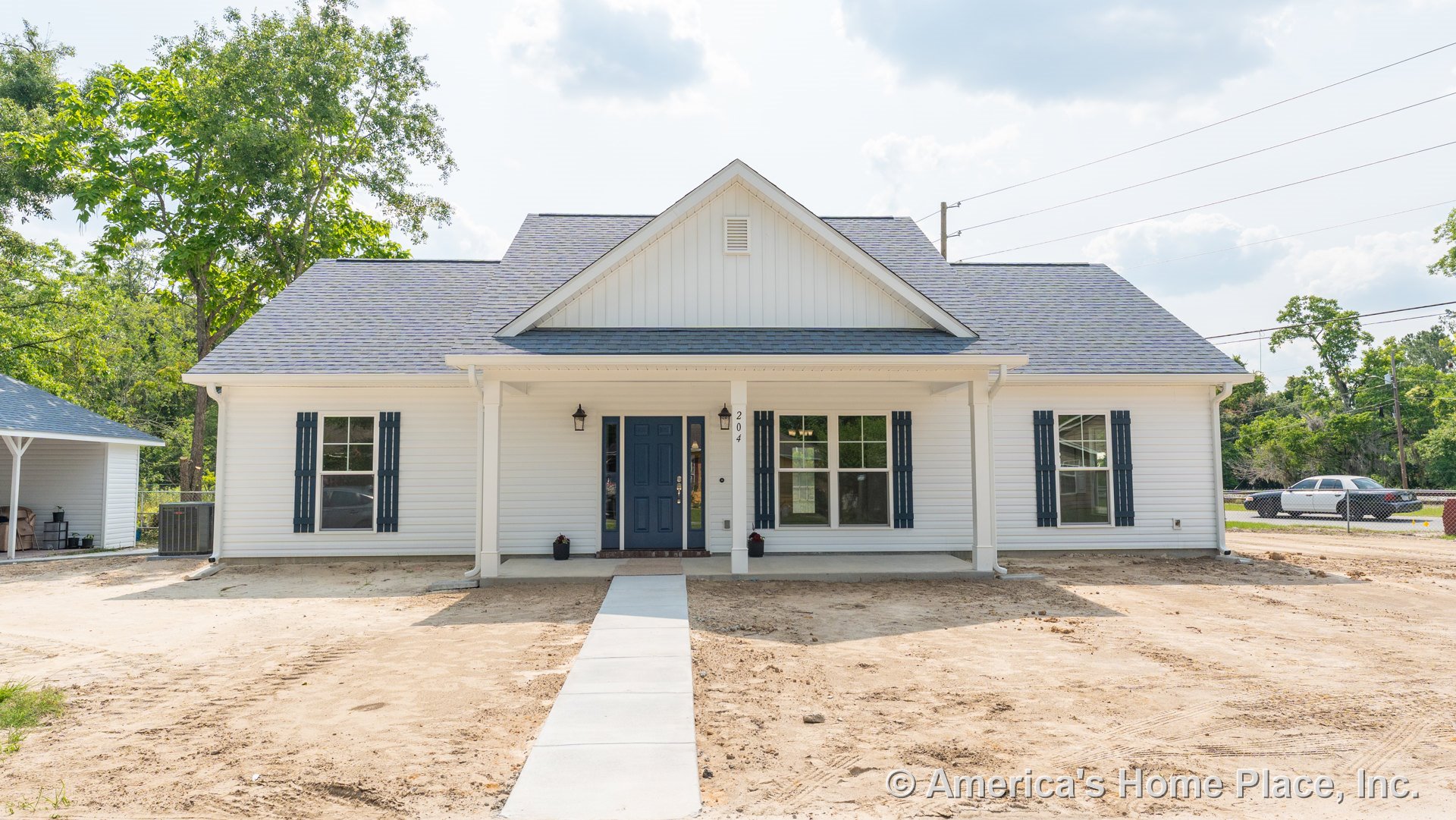 Covered front porch with white horizontal siding, blue front door, double-hung windows framed by blue shutters, exterior wall-mounted lanterns, gable roof, and paved walkway.