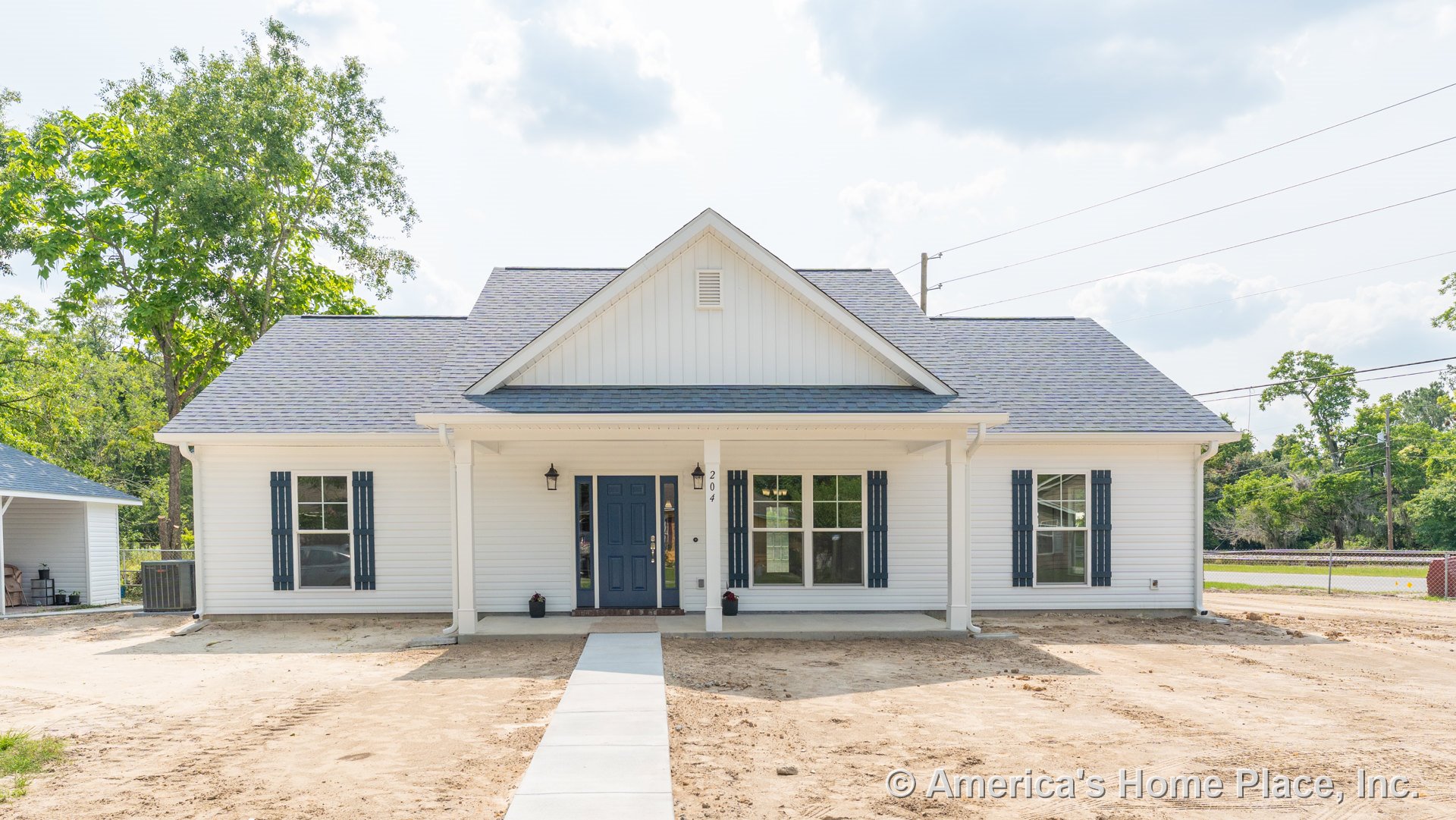 Covered front porch with white horizontal siding, blue front door, blue window shutters, gable roof, concrete walkway, white columns, and exterior lighting.