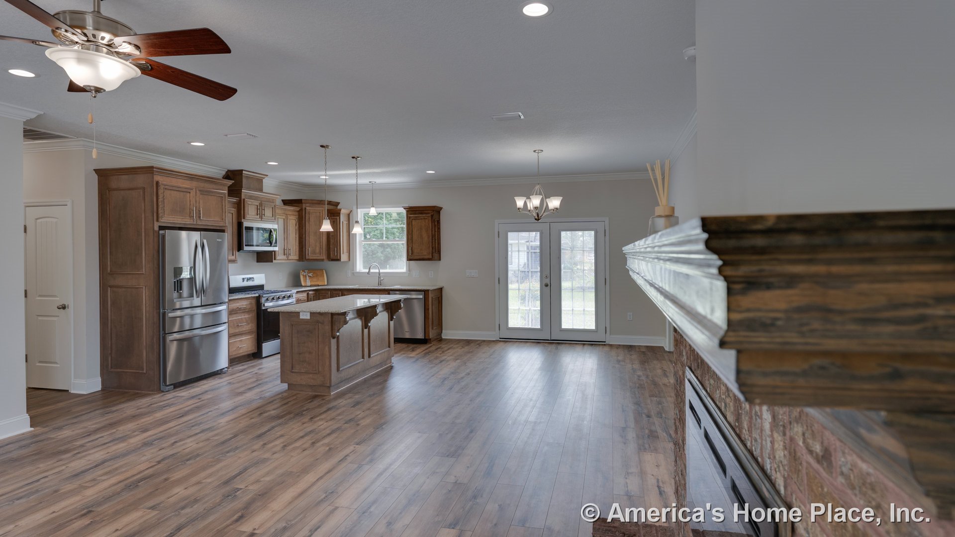 Open kitchen and living area with wood cabinetry, center island featuring decorative corbels, brick fireplace with wood mantel, French doors with glass panes, pendant and