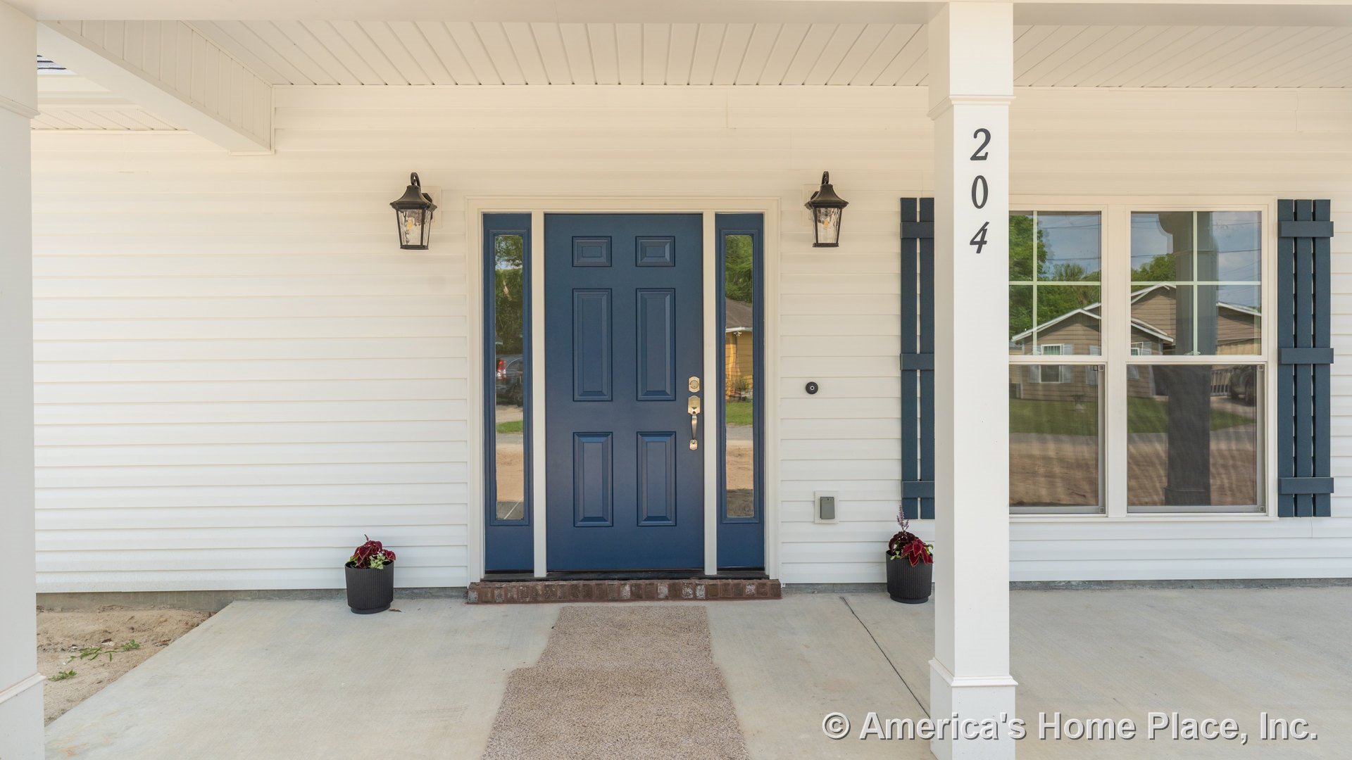 Covered front porch with blue entry door, matching blue window shutters, white vinyl siding, brick door step, built-in porch lighting, columns, house number, and concrete flooring.