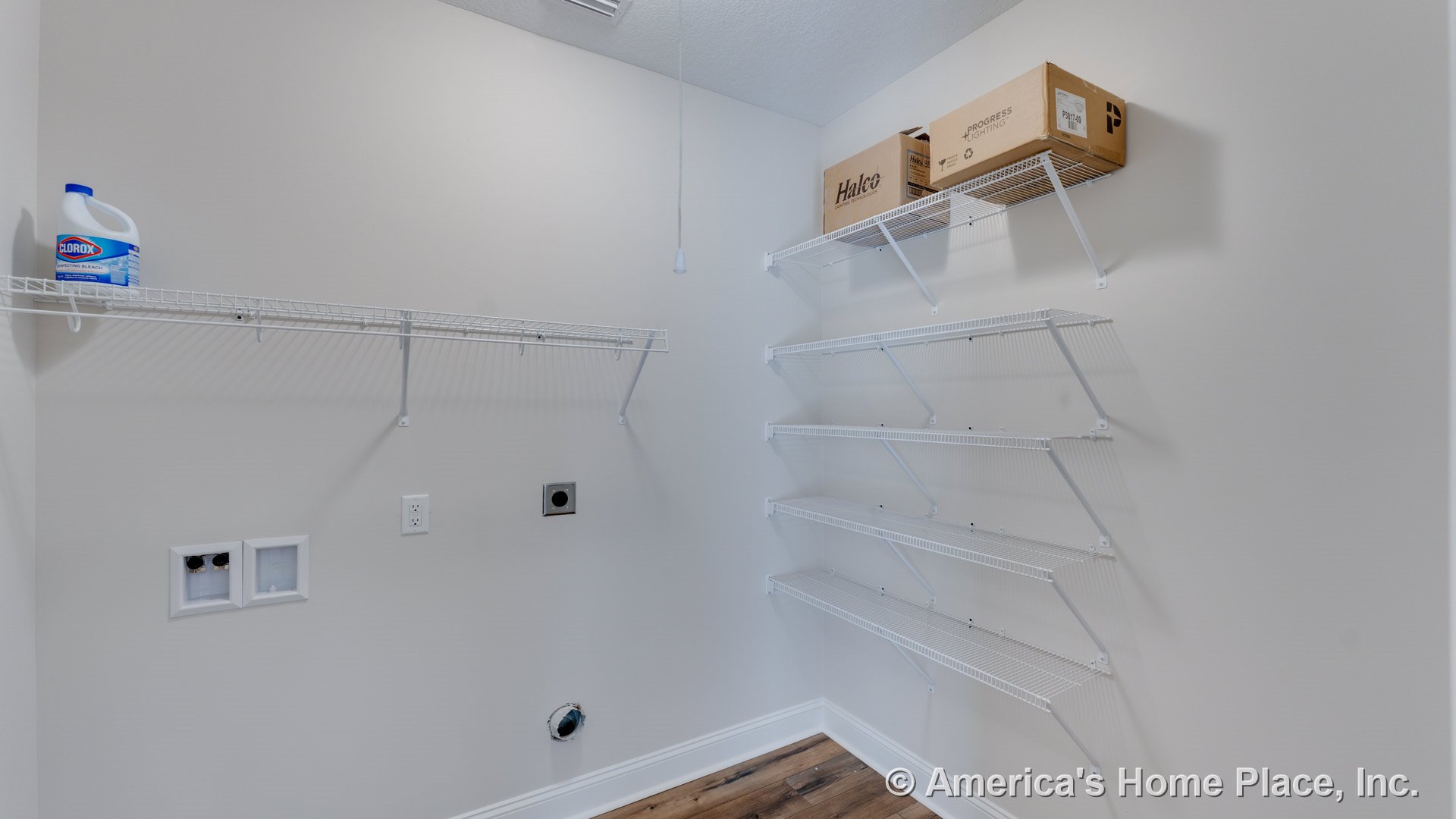 Laundry room with multiple white wire shelves, washer and dryer hookups, light beige walls, wood-look vinyl flooring, baseboard trim, and ceiling pull chain fixture.