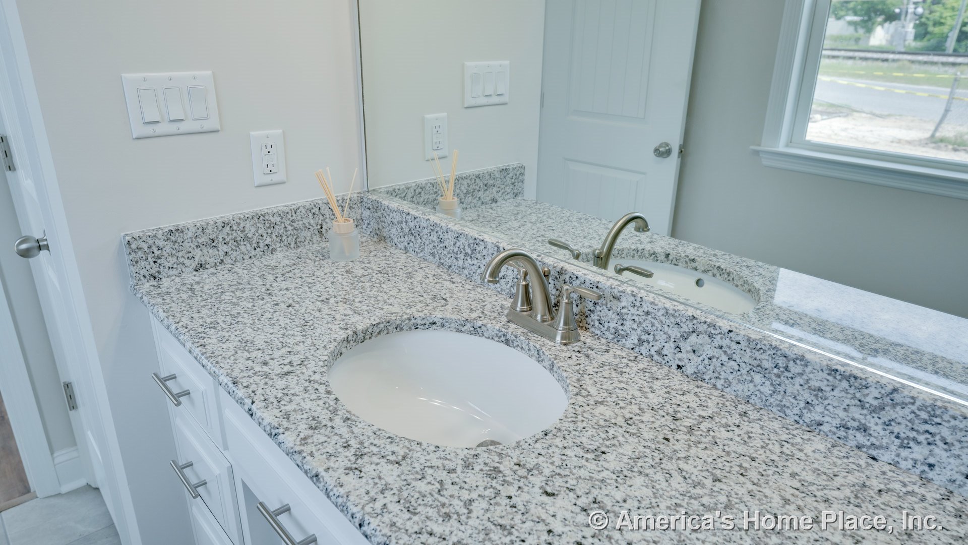 Granite vanity with oval undermount sink and brushed nickel faucet, large wall mirror above white shaker cabinets, window with trim, neutral wall color, built-in fixtures.