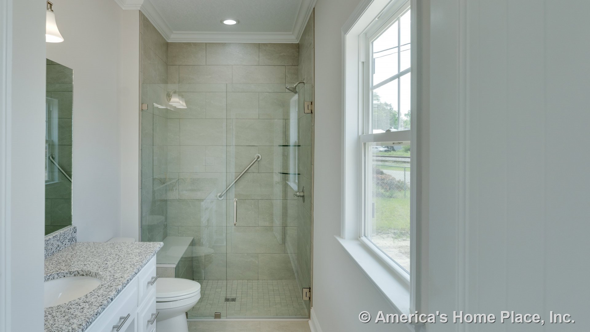 Glass-enclosed shower with large beige wall tiles, granite countertop vanity with white cabinetry, built-in shelves, shower grab bar, window with trim, recessed ceiling light