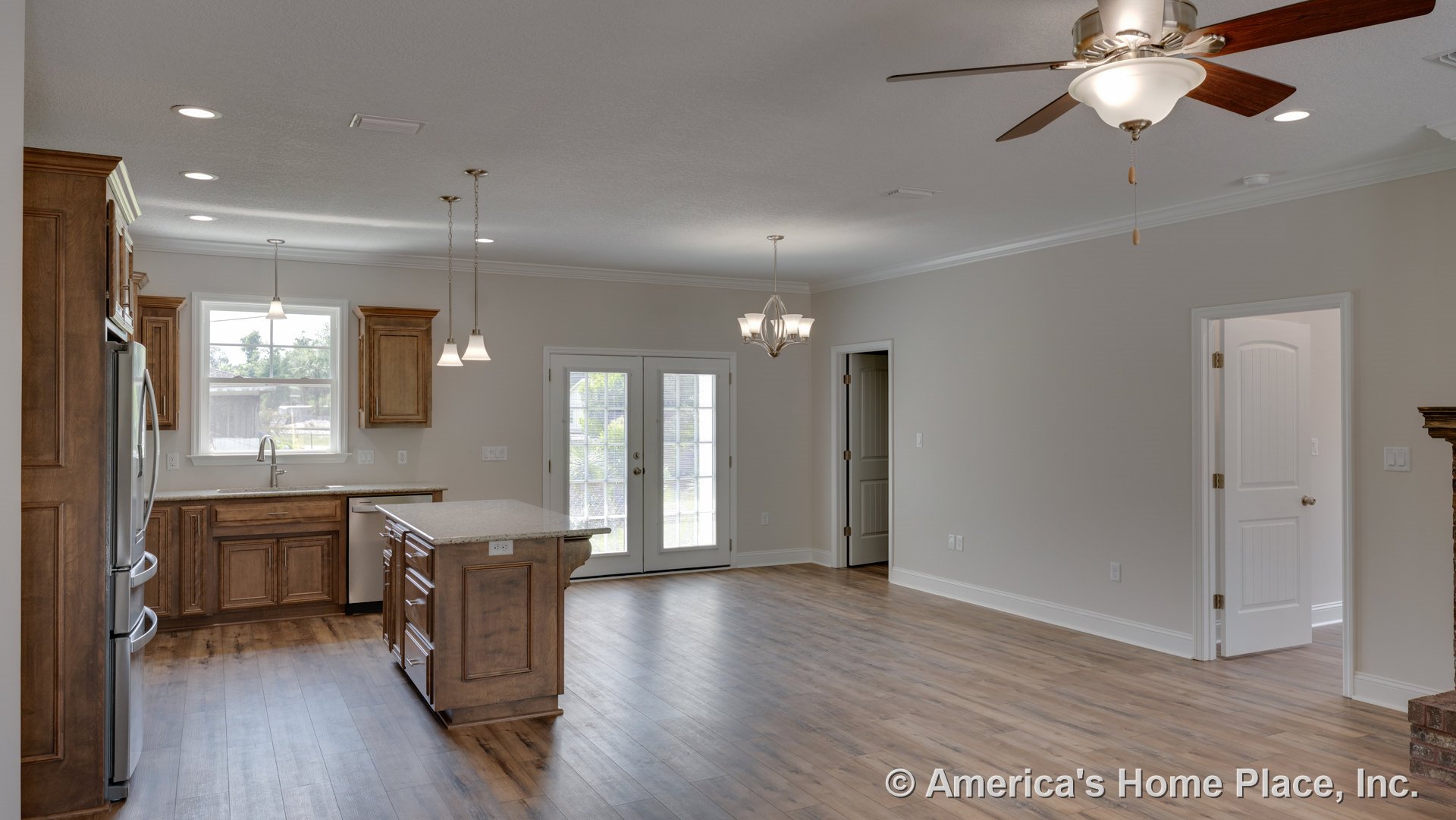 Open kitchen and living area with wood cabinetry, granite island countertop, pendant and chandelier lighting, French doors with glass panes, wide plank wood flooring, ceiling fan