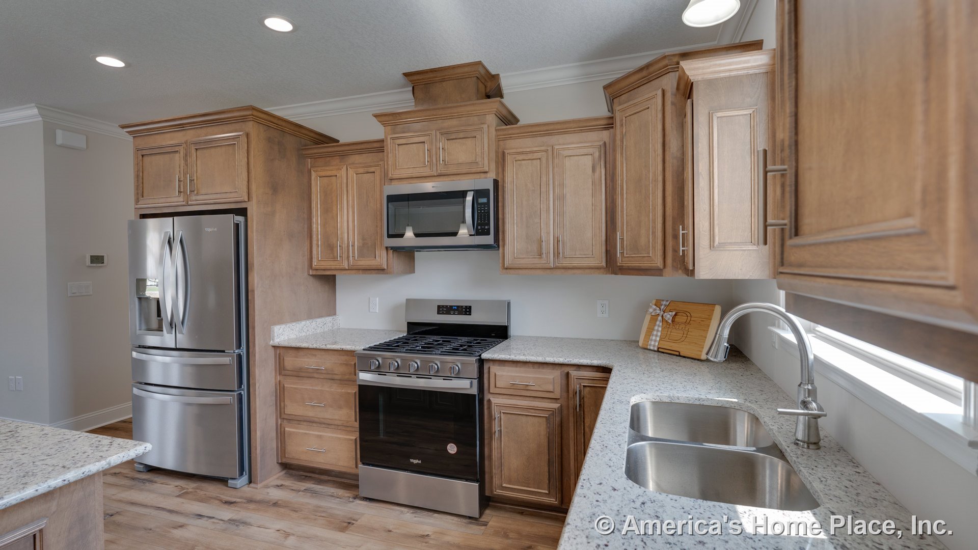 Wood cabinetry with upper and lower storage, granite countertops, stainless steel refrigerator and gas range, built-in microwave, double basin undermount sink with modern faucet