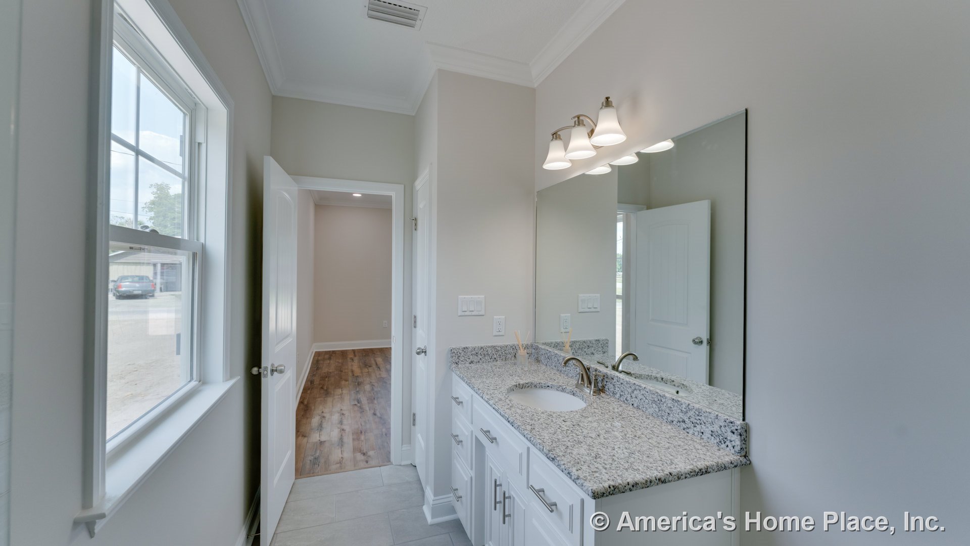 Granite vanity top with single undermount sink, white shaker cabinets, expansive wall mirror beneath three-light fixture, neutral tile flooring, trimmed window, crown molding, and