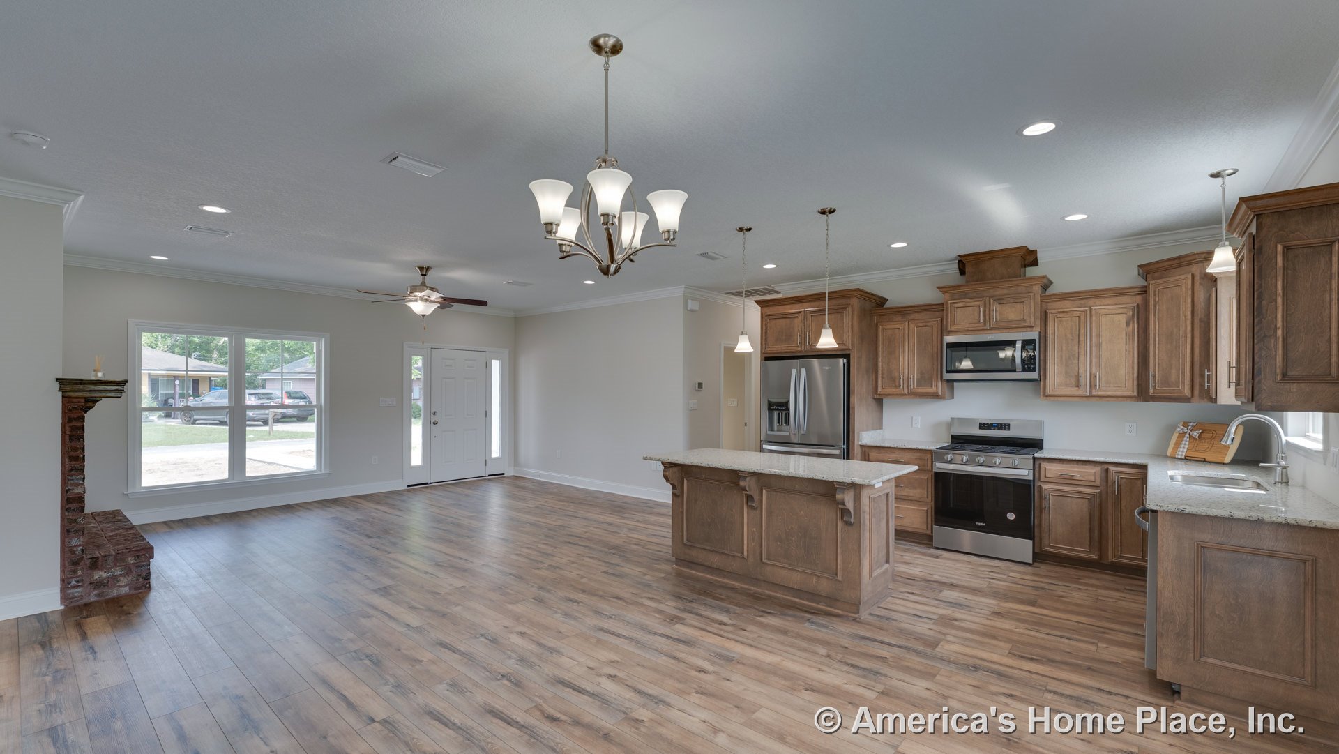 Open kitchen and living area with wood cabinetry, granite countertops and island, stainless steel appliances, wide plank flooring, large front windows, brick fireplace hearth