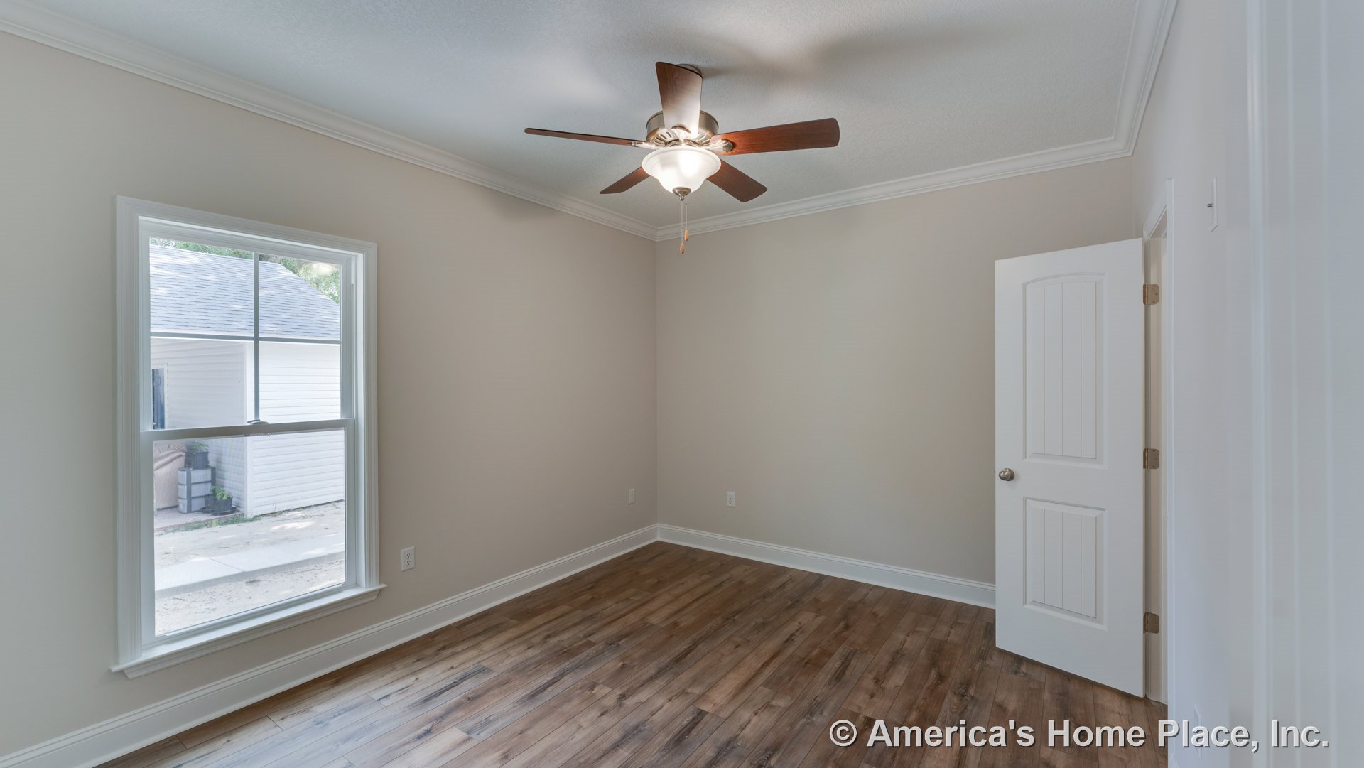 Bedroom with wood-look plank flooring, ceiling fan and light fixture, large double-hung window, white crown molding, neutral wall paint, paneled interior door, and baseboard trim.