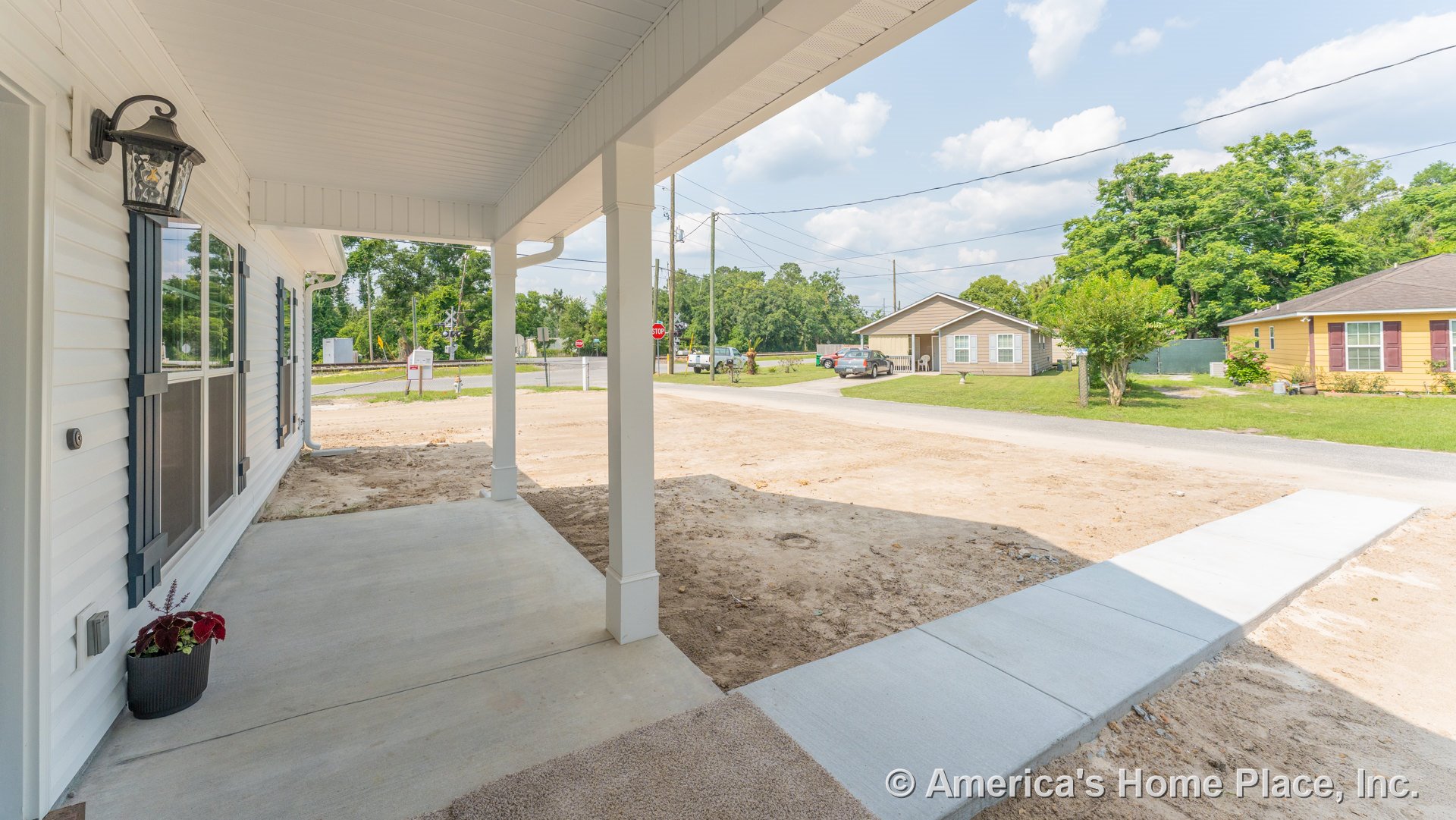 Covered front porch with concrete flooring, white vinyl siding, black outdoor lantern, double window with shutters, sidewalk leading to porch, white trim, and columns at the entry.