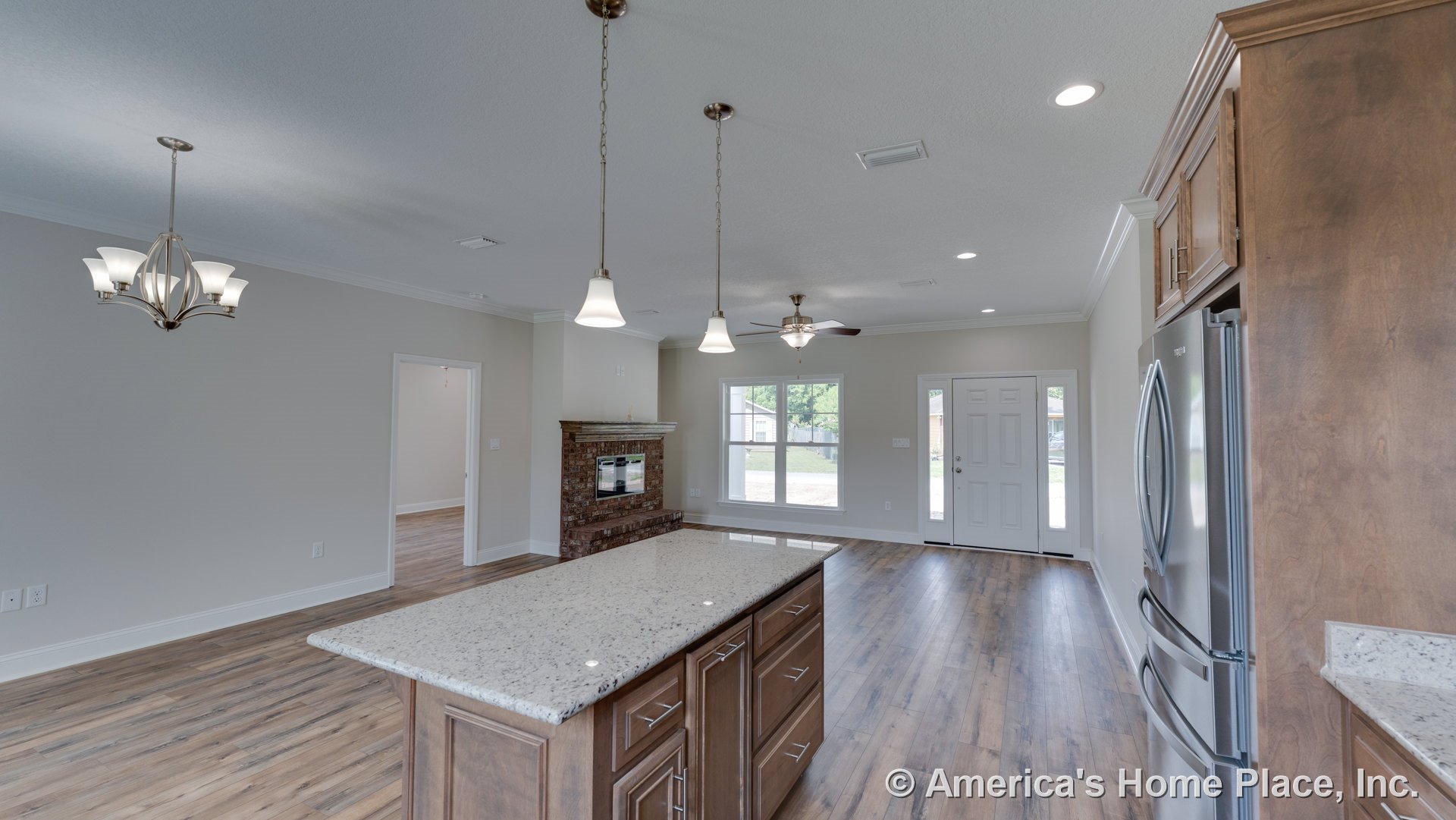 Open kitchen and living area with wood cabinetry, granite countertops, pendant lighting, brick fireplace, large windows, wood-look flooring, stainless steel appliances, and open