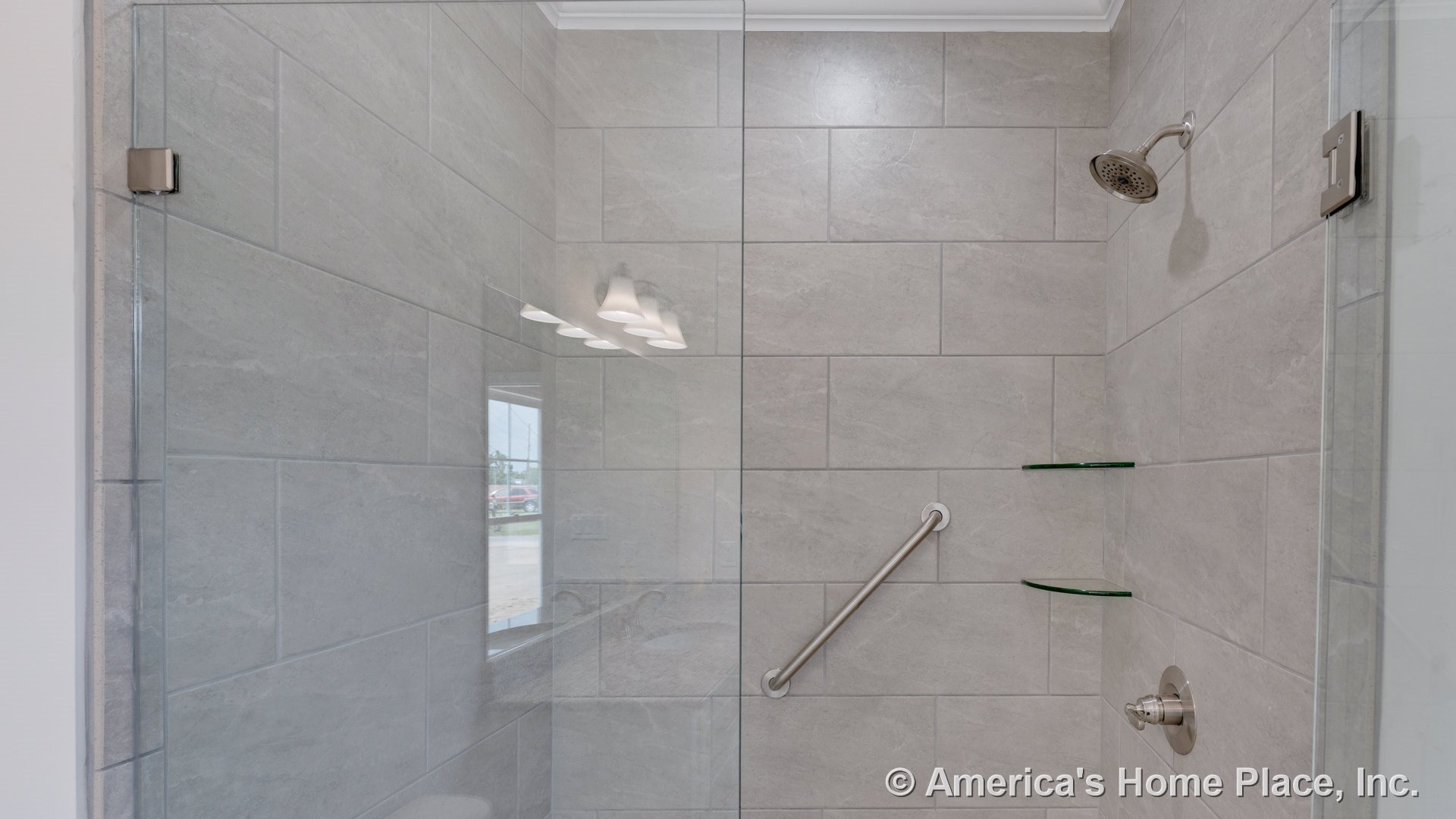 Large-format gray tile shower walls with a glass enclosure, built-in glass corner shelves, metal grab bar, chrome showerhead, and recessed shower controls.