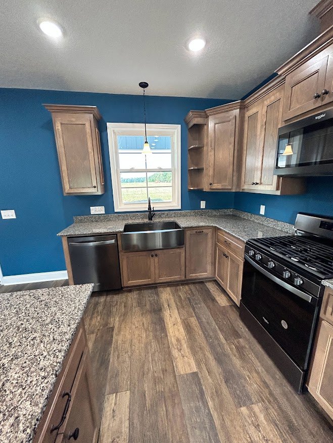 Kitchen with blue painted walls, wooden flooring, stainless steel stove, microwave, silver pot on the counter, and built-in dishwasher beneath white cabinetry