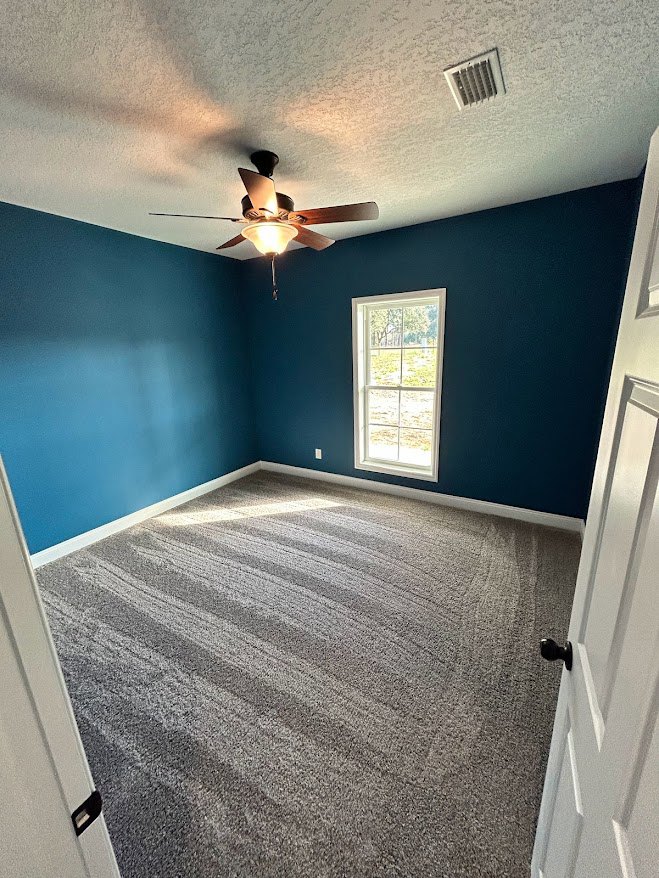 Carpeted room with white plaster walls, ceiling fan with light fixture, and wooden door