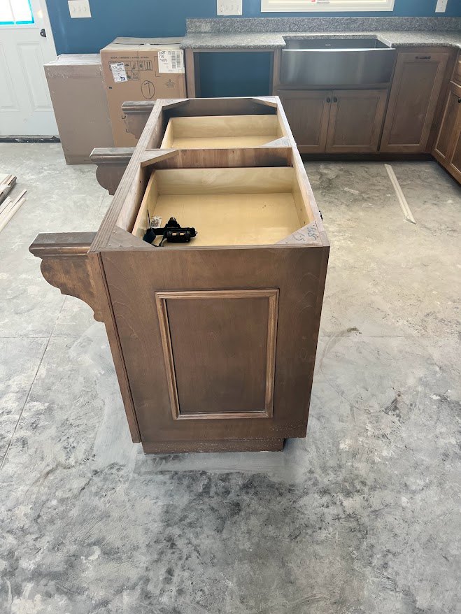 Wood kitchen cabinet with open shelf, silver microwave, cardboard box with label, white door against blue wall, concrete floor with white line