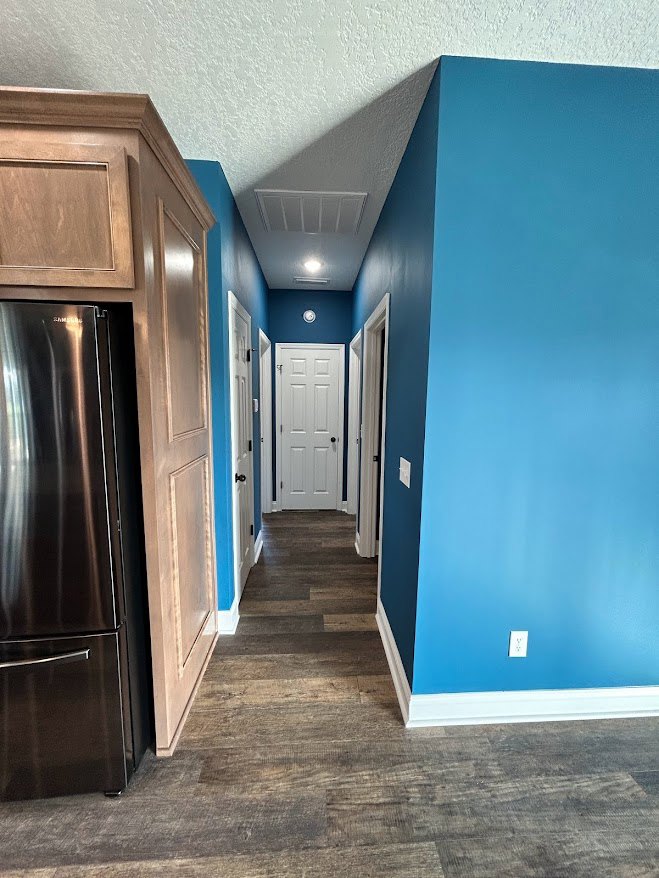 Hallway with matte blue walls, white paneled doors featuring black trim, light wood flooring, and silver door hardware