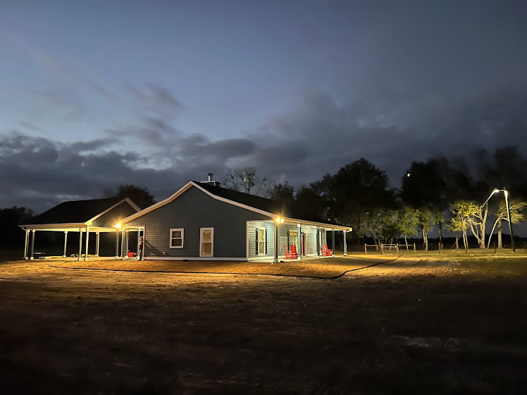Two-story house with covered porch, white picket fence, manicured lawn, and mature trees under a cloudy evening sky
