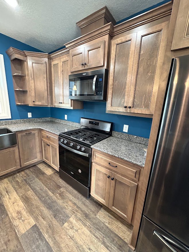 Kitchen with black stove, stainless steel refrigerator, granite countertops, white cabinetry, built-in microwave, and under-cabinet lighting