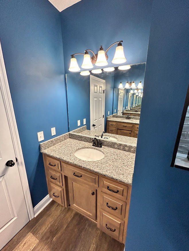 White bathroom with rectangular mirror above a stone countertop sink, modern chrome faucet, light wood cabinetry, and tiled walls