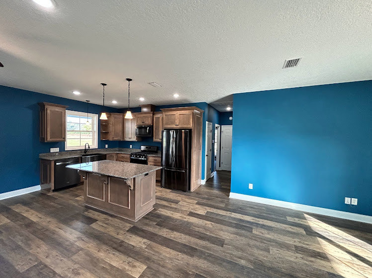 Kitchen featuring a bold blue accent wall, light wood flooring, stainless steel refrigerator, white cabinetry, stone countertops, and modern fixtures