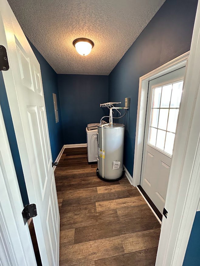 Wood floor room with white framed window, white door featuring glass panel, ceiling light fixture, and silver cylindrical object near wall