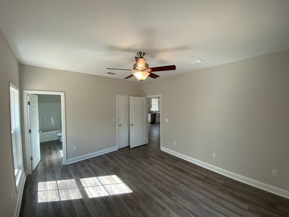 Ceiling fan with light fixture above wood laminate flooring, white door with silver knobs, plaster walls, natural light illuminating floor.