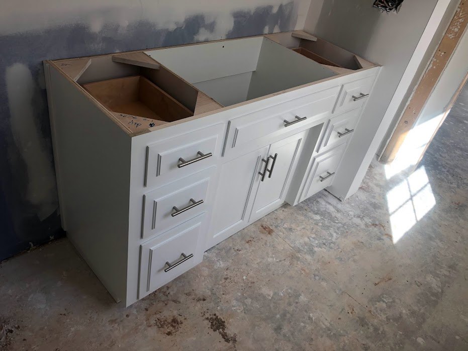 White kitchen counter with multiple drawers and metal handles, sunlight streaming through nearby window, close-up of white cabinetry and wall.