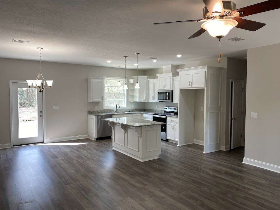 Open kitchen and dining area featuring a white kitchen island with marble countertop, glass panel door, chandelier, ceiling fan with light fixture, white cabinetry, and hardwood