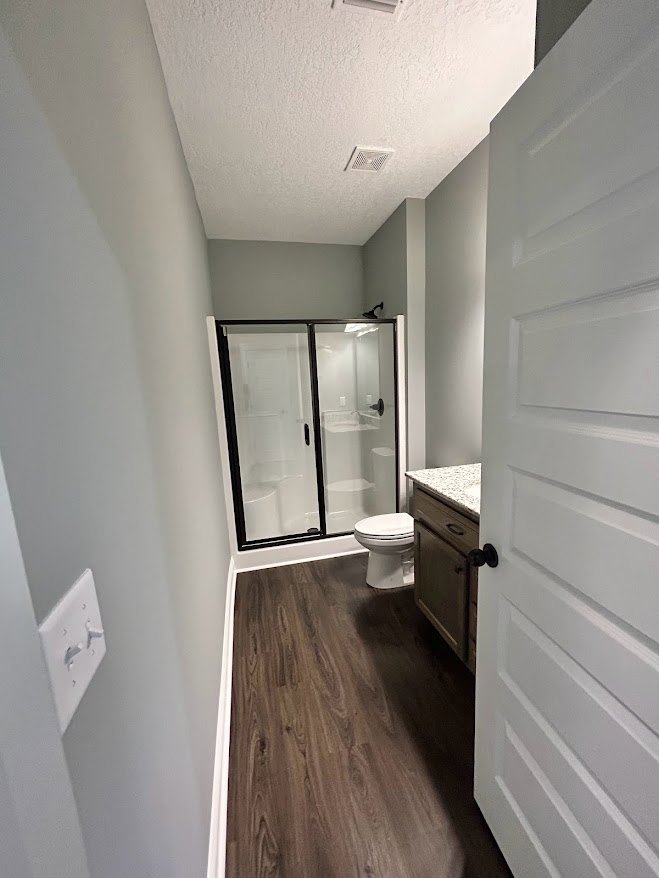 Modern bathroom featuring a glass-enclosed shower, white toilet, and sleek white countertop with wood cabinetry, light plaster walls, and hardwood flooring