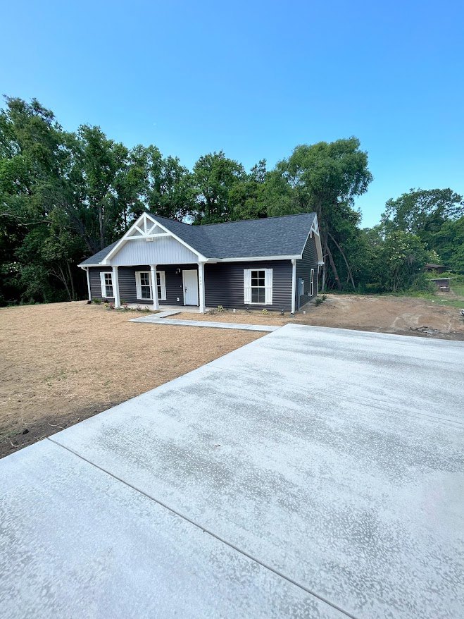 Two-story house with white trim and windows, concrete driveway and walkway, mature trees in the background, blue sky overhead