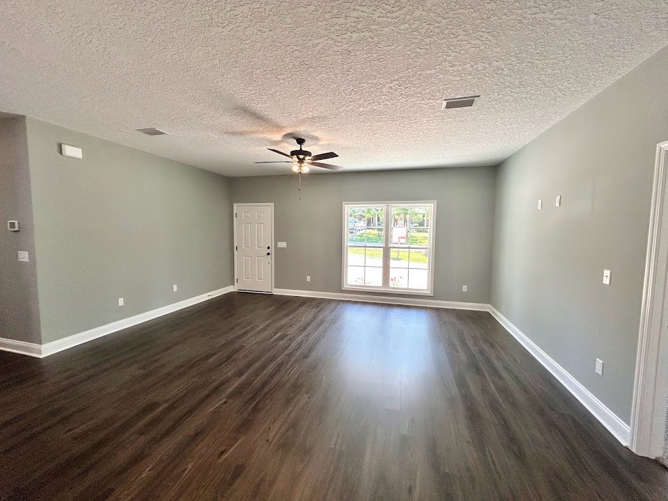 Hardwood floor room with white walls, ceiling fan with light, large window overlooking yard, and white door with black handles