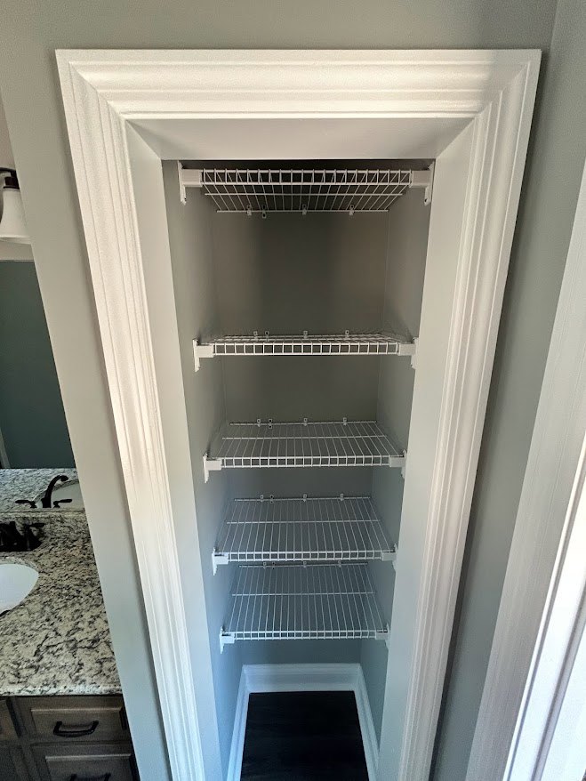 White closet with built-in shelves against a smooth wall, featuring organized storage spaces and neutral finishes.
