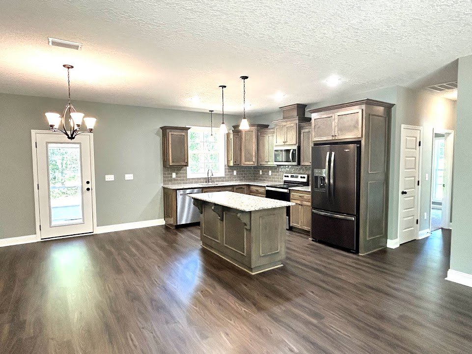 Open kitchen and dining area with wood flooring, marble-topped island, stainless refrigerator, white cabinetry, and glass-paneled door