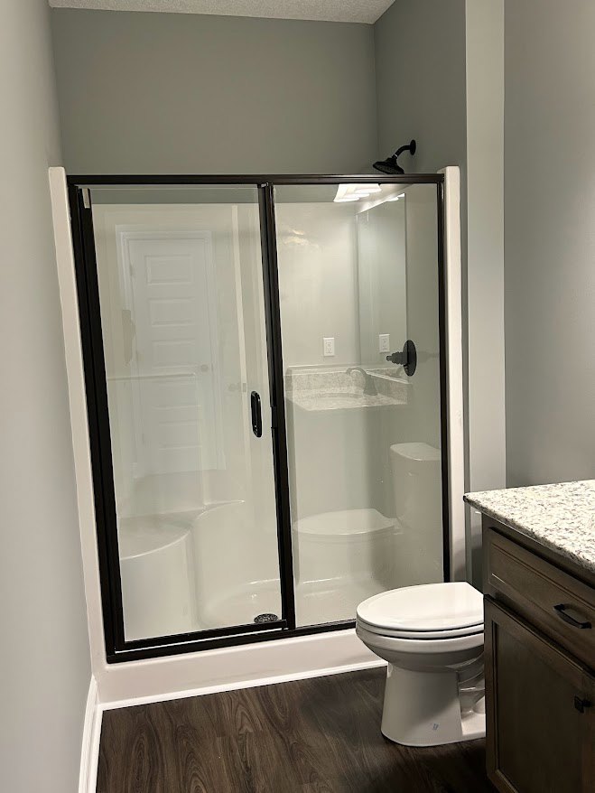 Bathroom featuring a glass shower door, marbled countertop with sink and chrome faucet, white toilet, light-colored tile walls, and wood cabinetry