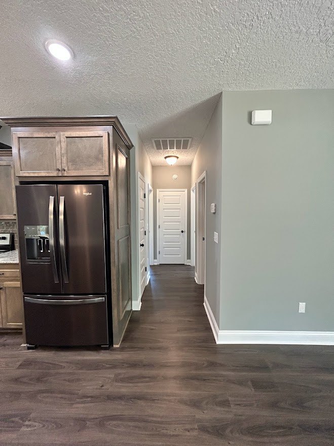 Kitchen with stainless steel refrigerator, white cabinetry, black hardware, and dark wood flooring