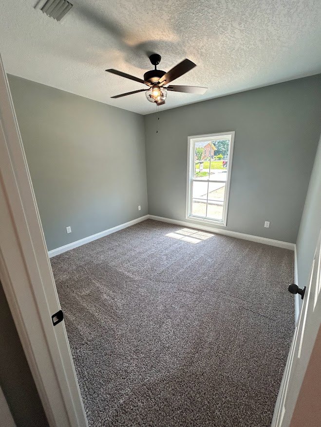 Bedroom with beige carpet, white walls, ceiling fan with light, and window framed in white trim
