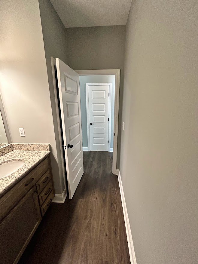 Bathroom with white laminate flooring, plaster walls, modern sink vanity, wood cabinetry, and a closed door.
