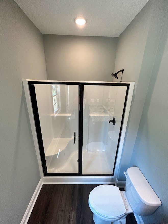 Bathroom with tiled walls, glass-enclosed shower, wall-mounted toilet, large mirror, and chrome fixtures