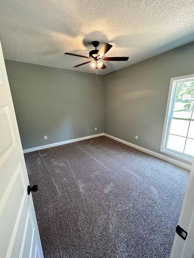 Carpeted bedroom with white-framed window, ceiling fan with light fixture, neutral walls, and crown molding