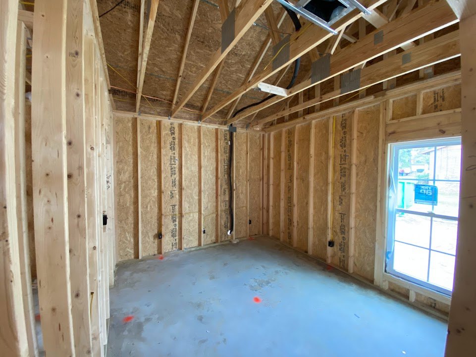 Room with exposed wood ceiling beams, concrete floor, window with blue sign, and unfinished plaster walls