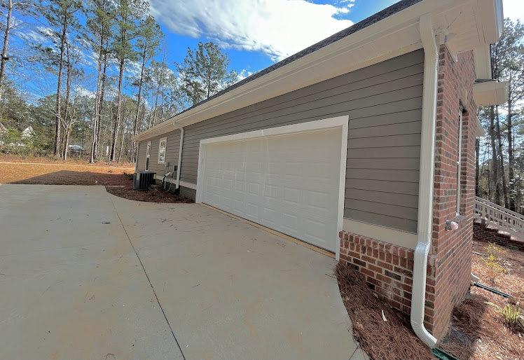 Two-story house with light-colored siding, attached garage, paved driveway, manicured lawn, mature trees, and partly cloudy sky