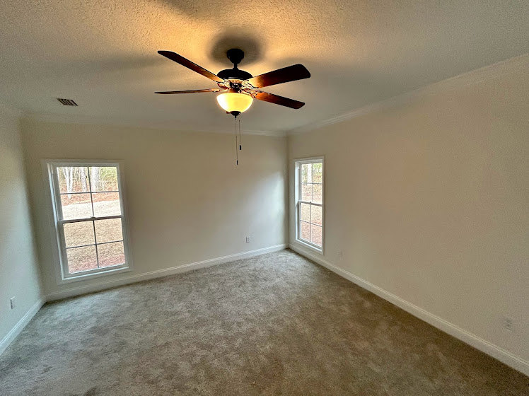 Ceiling fan with integrated light fixture mounted on white plaster ceiling in spacious room with large windows and hardwood floor