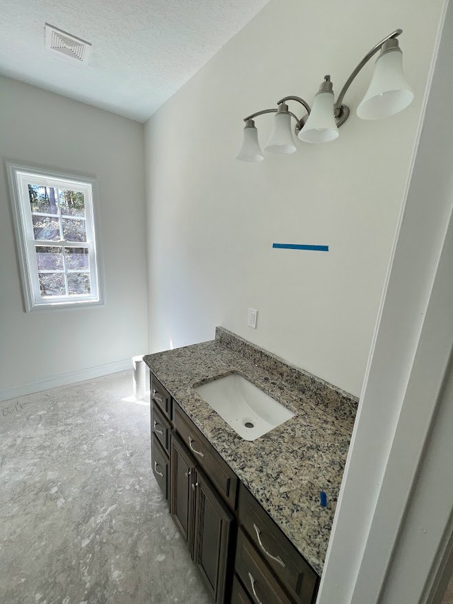 Bathroom with marble countertop, white undermount sink, chrome faucet, large mirror, white framed window, light tile flooring, and white cabinetry