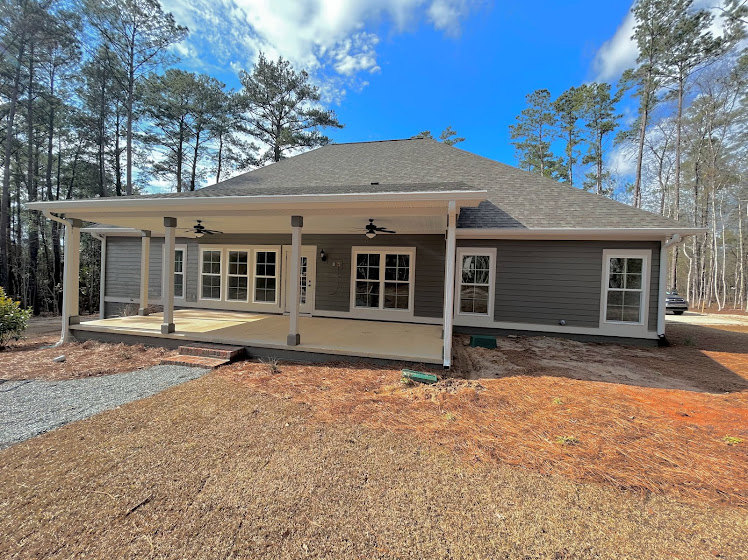 Two-story home with white siding, covered front porch featuring a ceiling fan, multi-pane windows, and landscaped yard with trees under a partly cloudy sky