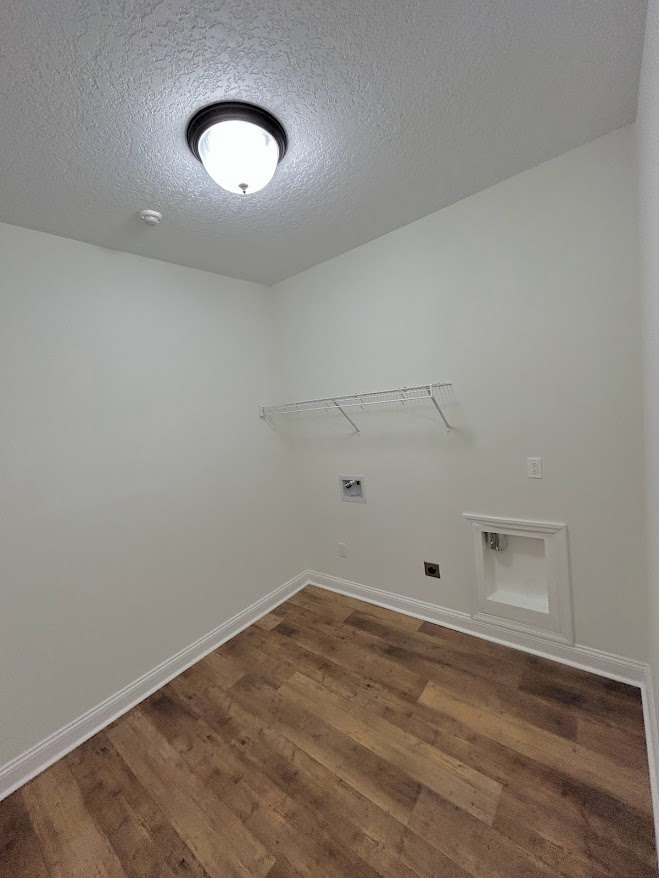 Open room with wood flooring, white walls, ceiling-mounted light fixture, built-in white cabinet, and white shelving.