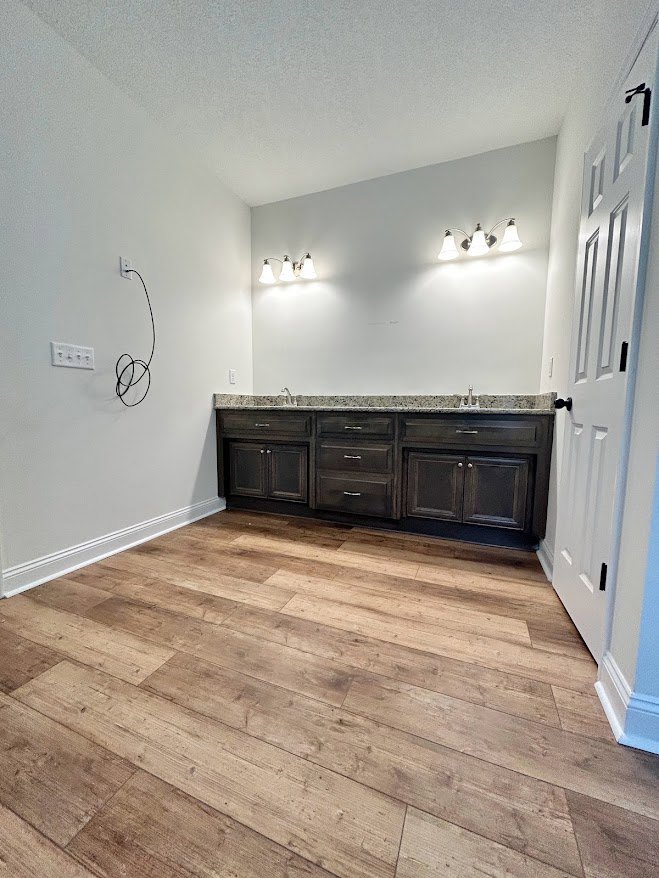 Bathroom with wood plank flooring, white paneled door featuring a black handle, white cabinetry, and plaster walls.