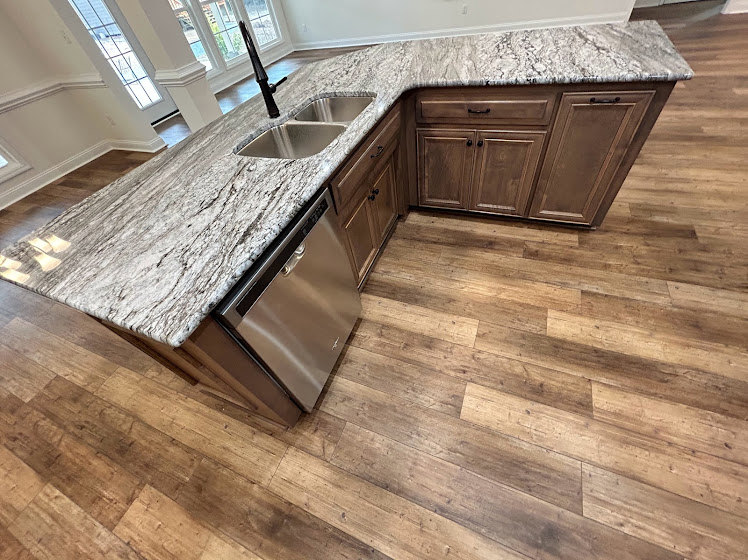 Granite countertop kitchen featuring stainless steel dishwasher, undermount sink, tile backsplash, wood cabinetry, and hardwood flooring