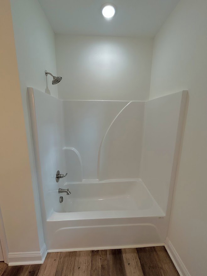 White bathtub with chrome shower head against tiled bathroom wall, plaster ceiling visible above, indoor plumbing fixtures and bathroom accessories present.